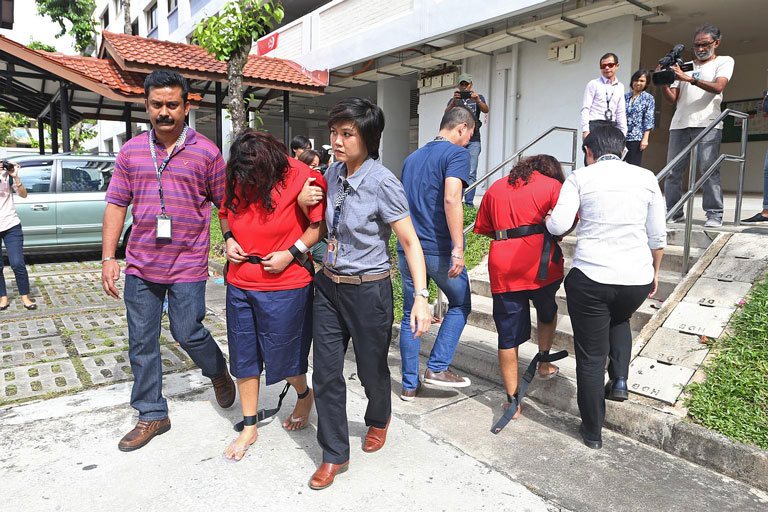 Police officers escorting Gaiyathiri Murugayan (left, in red) and her mother Prema Naraynasamy (right, in red) to their home
