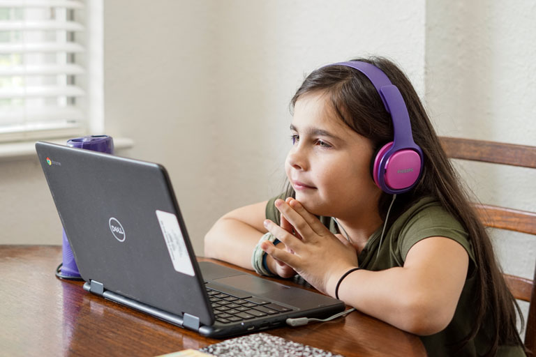 Young cute elementary aged girl with headphones on looking at a laptop