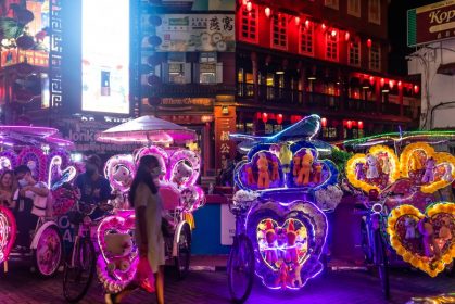 Woman walking across some colourful night carriages on a busy street at Melaka